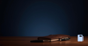 夜の静けさと安心感を感じるビジュアル。 暗めのネイビー背景、柔らかな間接照明の光。 静かな部屋、閉じたノートとペンが机に置かれている