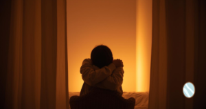 夜の室内、やわらかな灯り、腕で自分を包む仕草